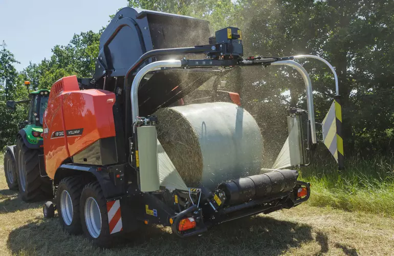 KUHN VBP 3260 baler-wrapper combination baling and wrapping bales under a blue sky.